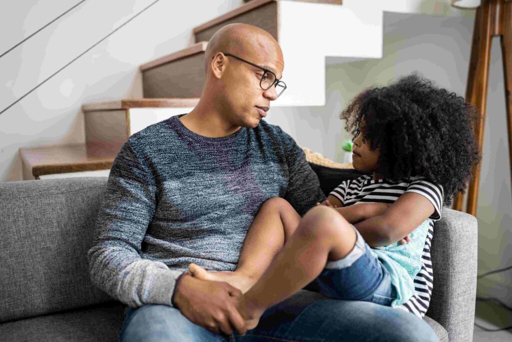 A parent and child talk on their living room couch.